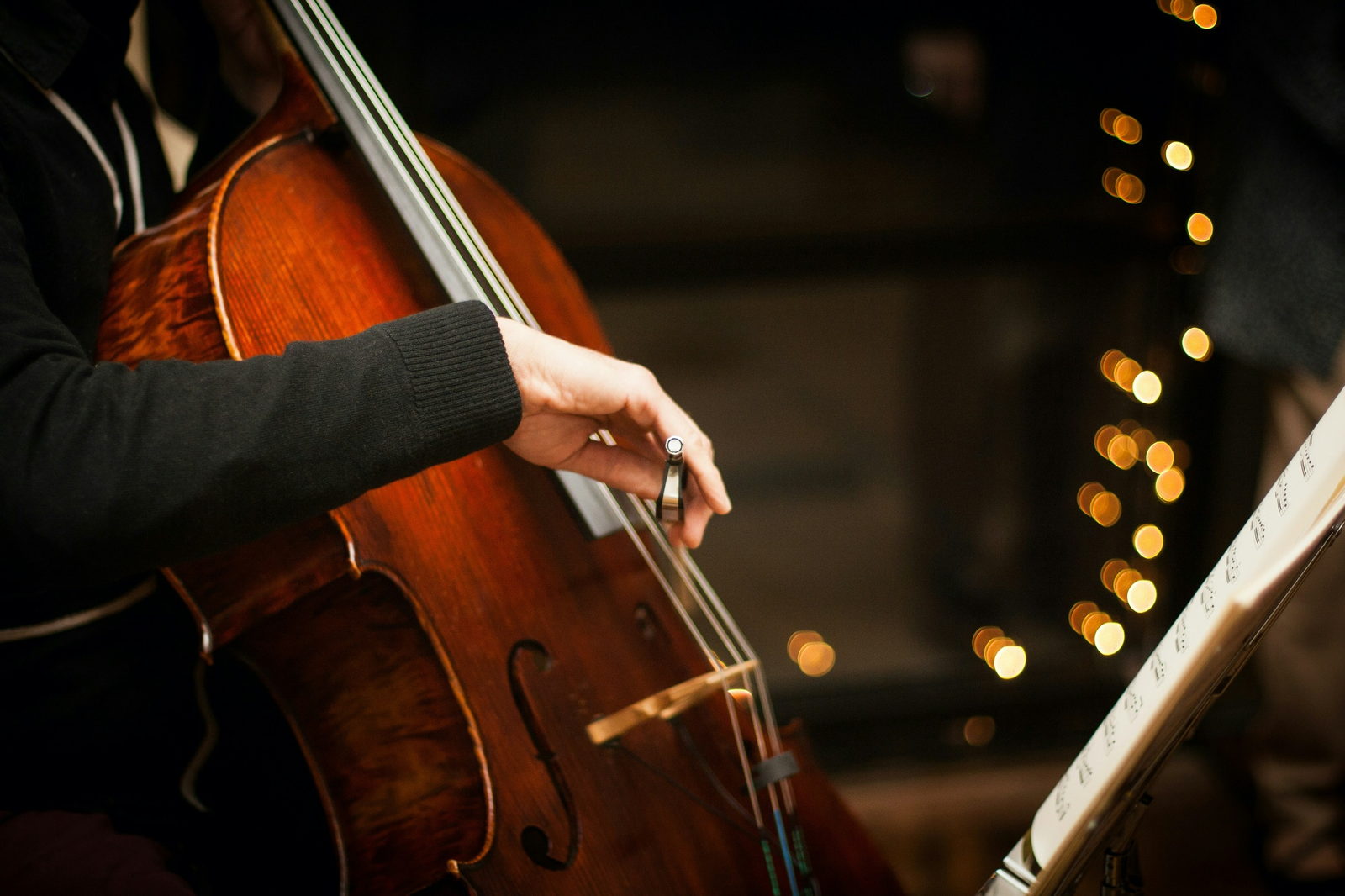 A cellist playing beneath strings of warm stage lights