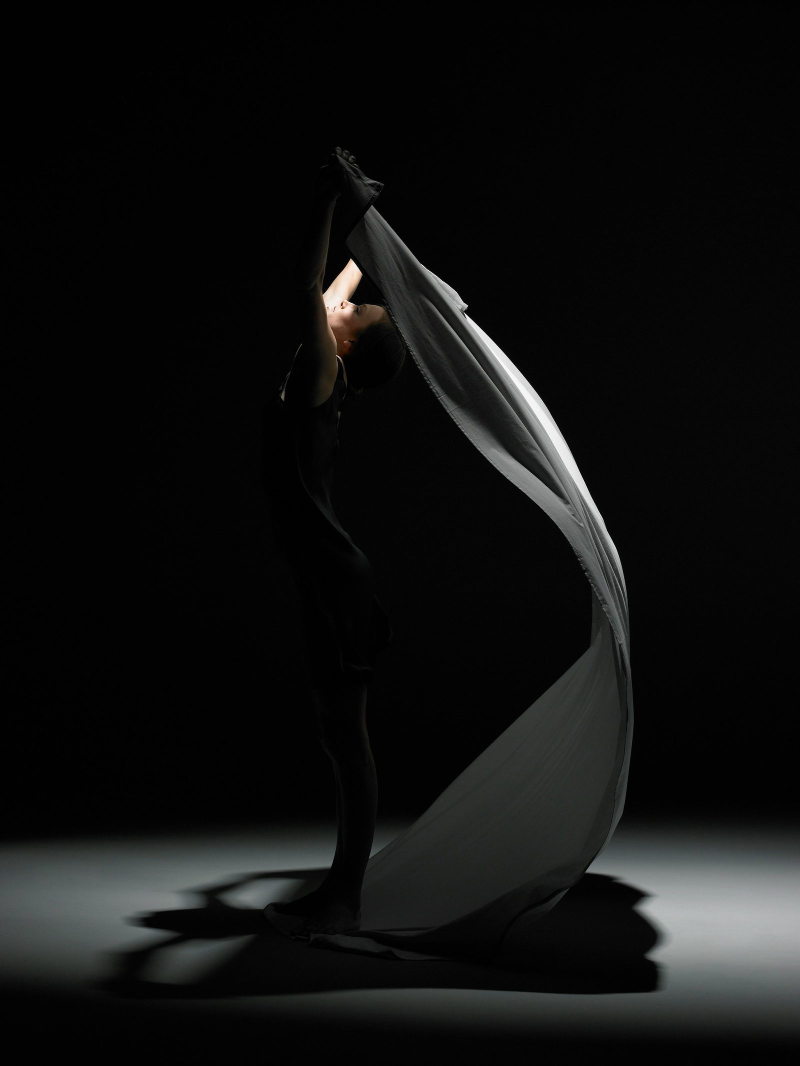 A dancer wrapped in flowing fabric against a black stage