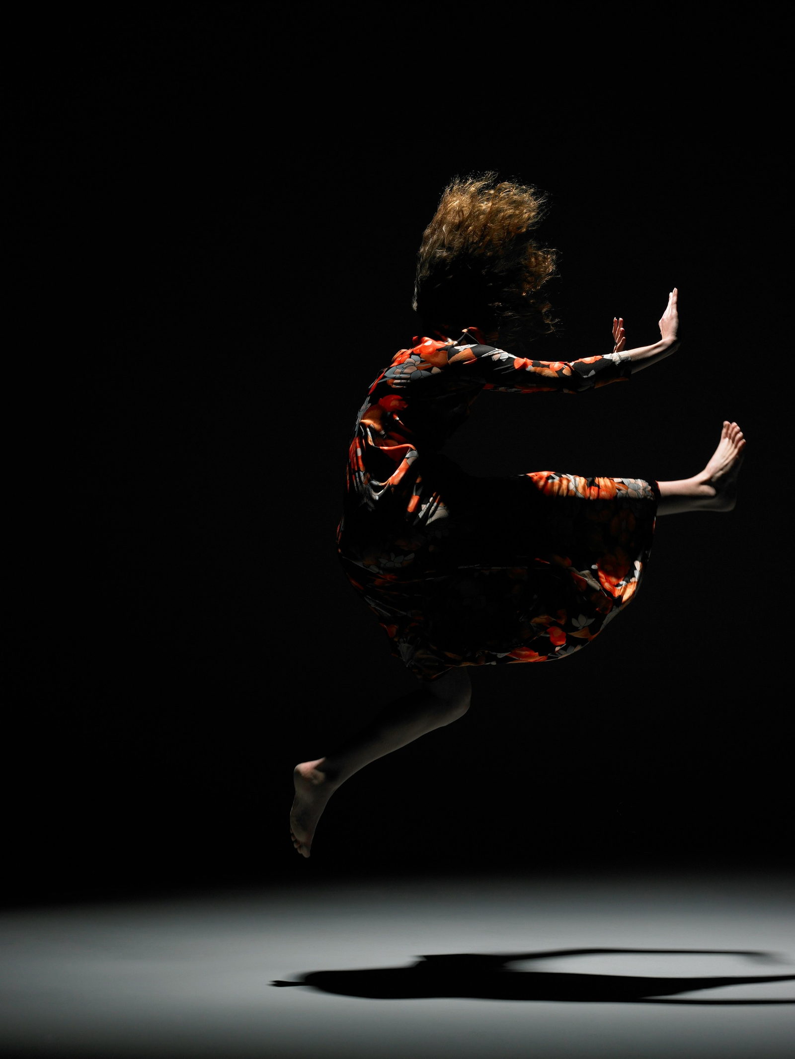 A dancer mid-leap in a floral dress against black