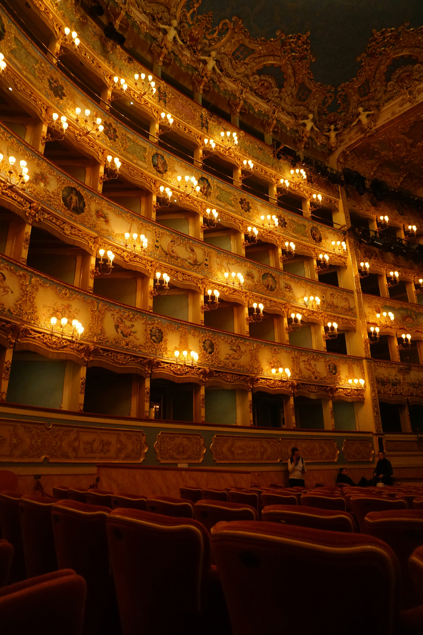 Gilded opera-house balconies above rows of red velvet seats