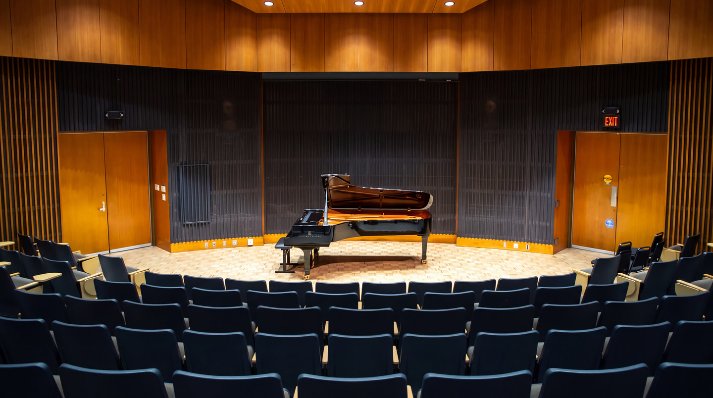 A grand piano on the stage of a wood-panelled recital hall
