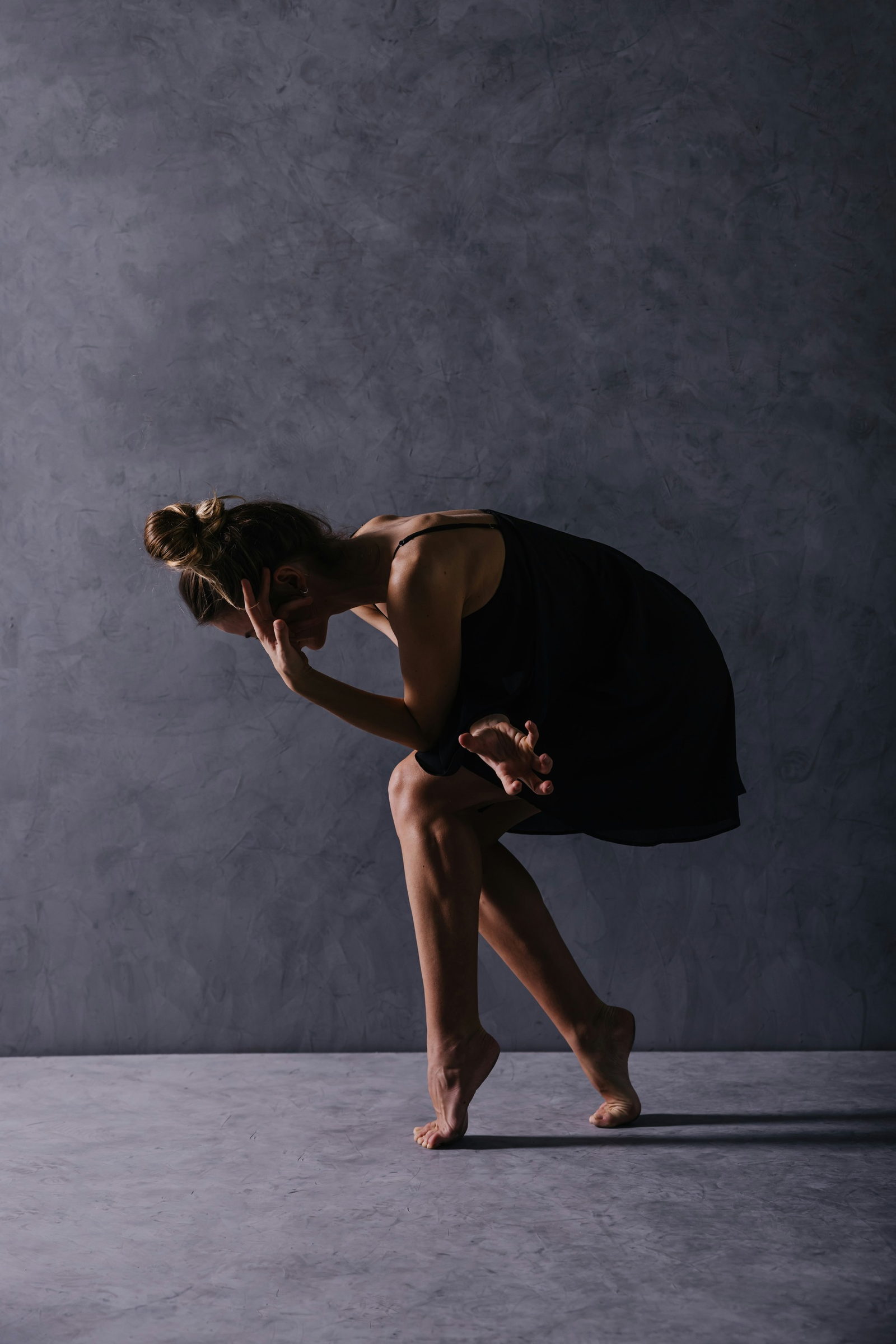 A solo dancer bowing low against a grey wall