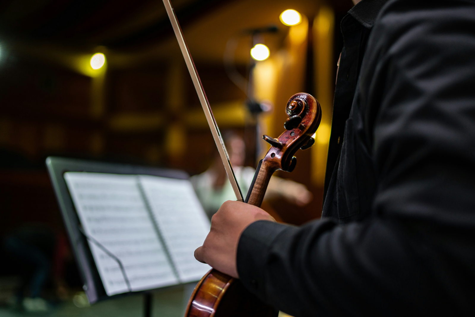 A violinist holding violin and bow beside a music stand on stage