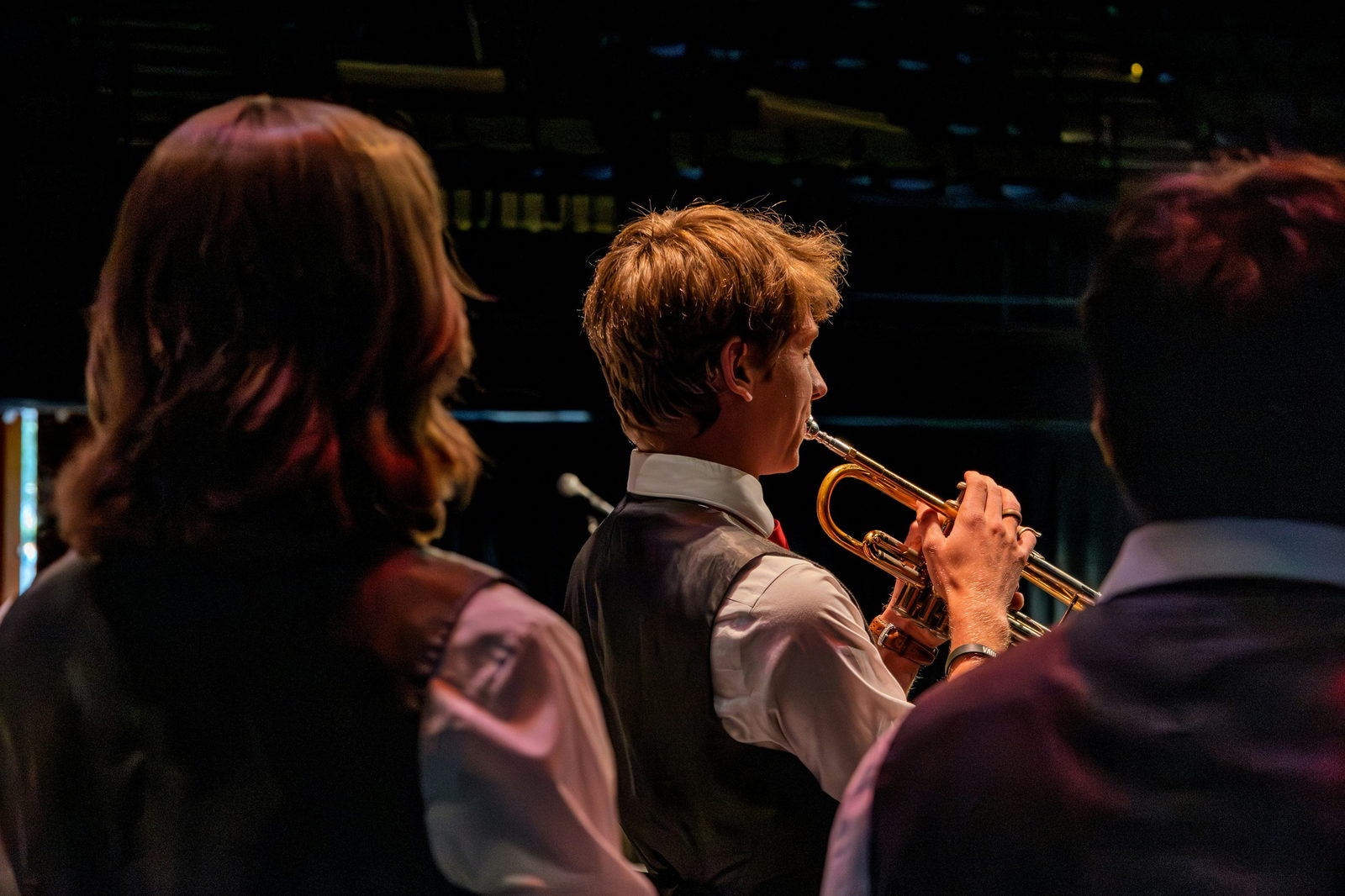 Young trumpet players in waistcoats performing on a dark stage