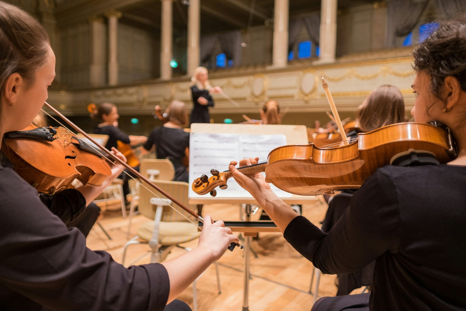 A youth string orchestra rehearsing in an ornate concert hall